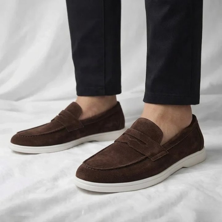 Pair of brown suede loafers with strap, stitched details, white rubber sole