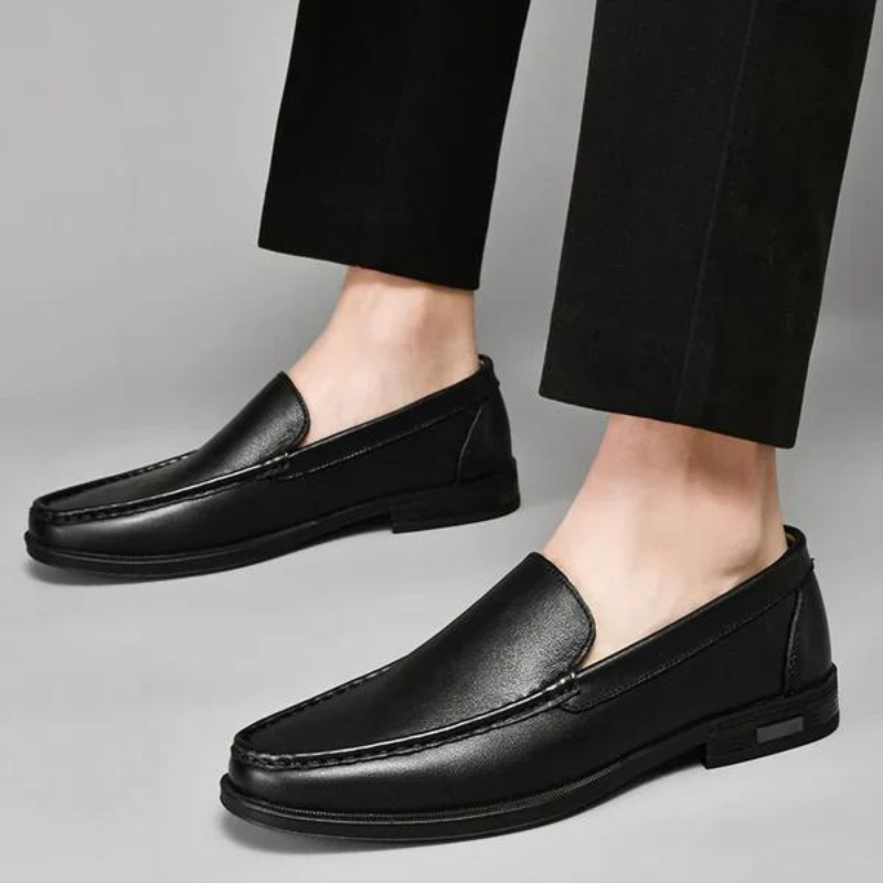Black leather penny loafers on a person with cropped pants, low-profile sole