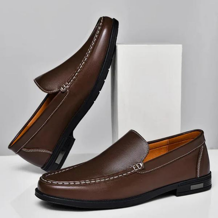 Brown leather penny loafer with stitched detail and metal bar, flat rubber sole