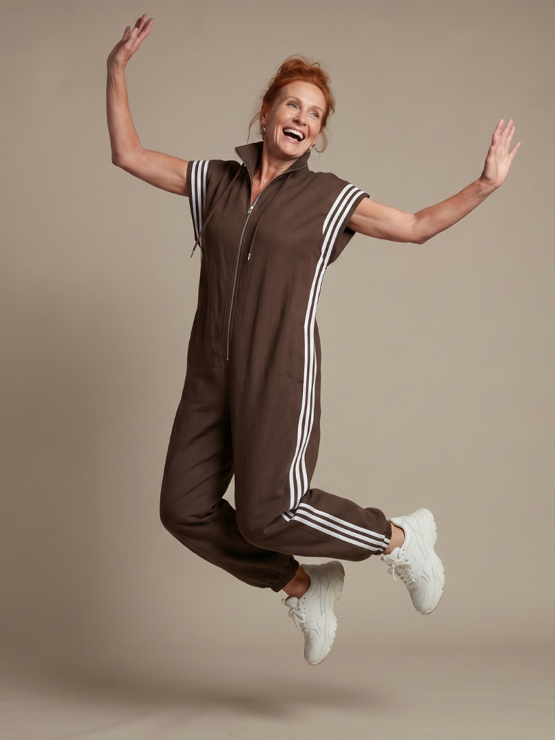 Brown sleeveless zip-front jumpsuit with white striped shoulder panels and drawstring hood