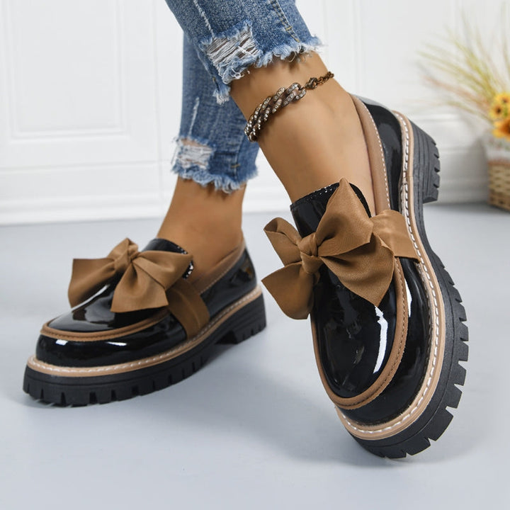 Black slip-on loafers with tan bow detail and chunky tread sole