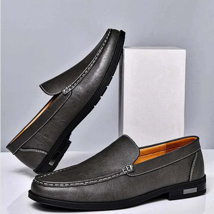 Dark gray leather loafer with metal bar strap, contrast stitching, and rubber sole