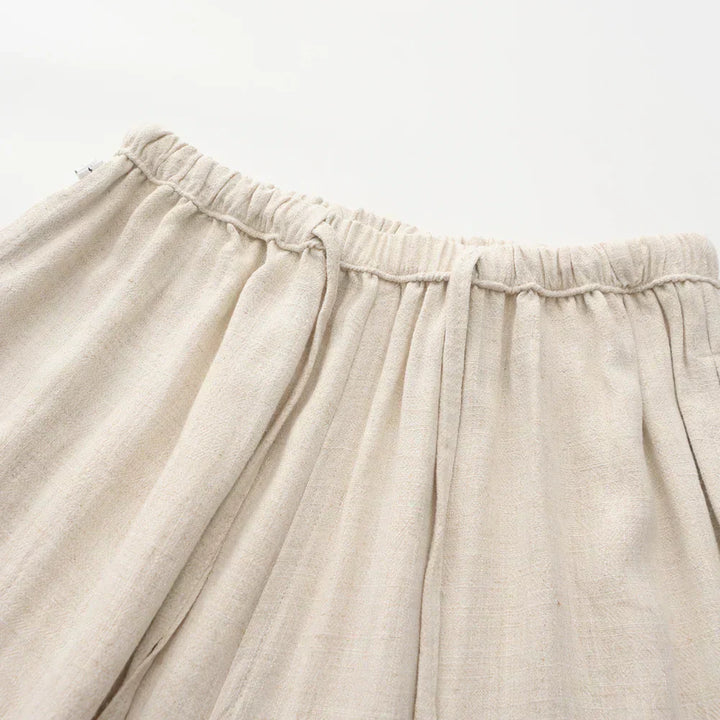 Beige linen pants waistband close-up with elastic gather and pleated front.