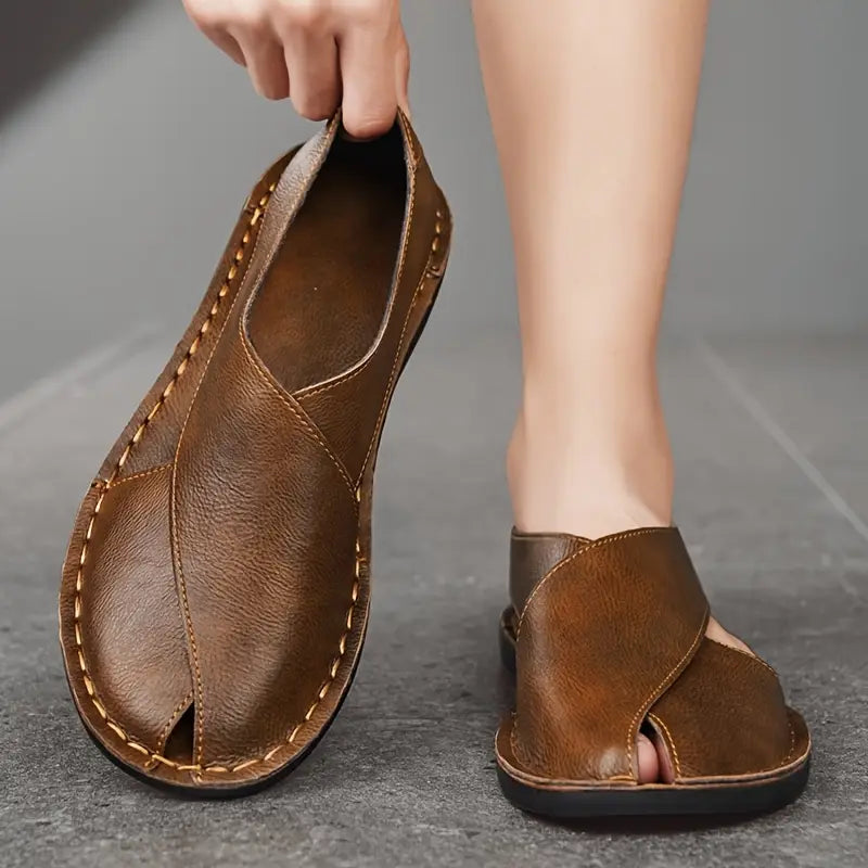 Brown leather open-toe slide sandal held up while another is worn on the other foot.