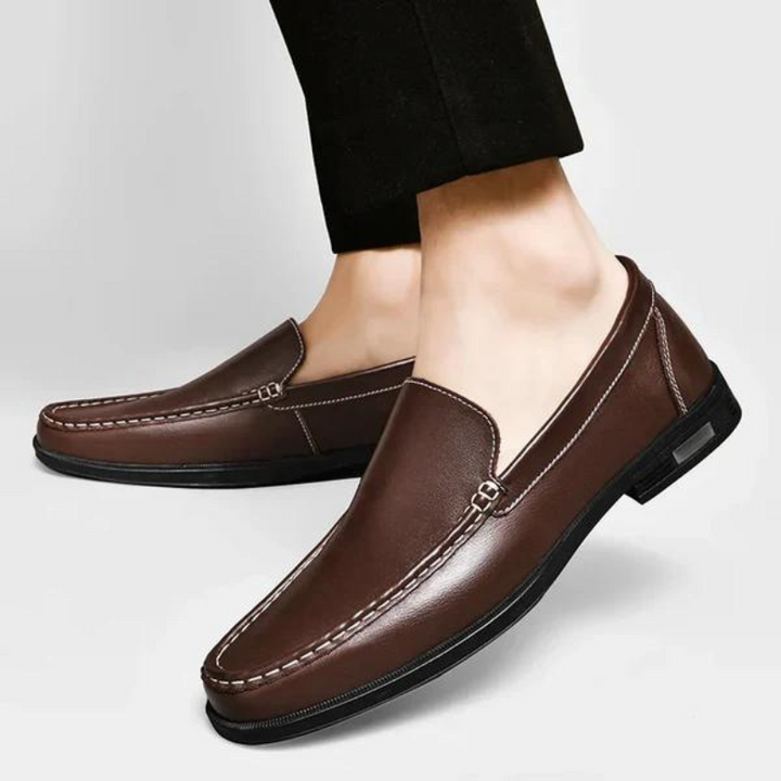 Brown leather penny loafers on feet, metal bar strap and stitched moc toe