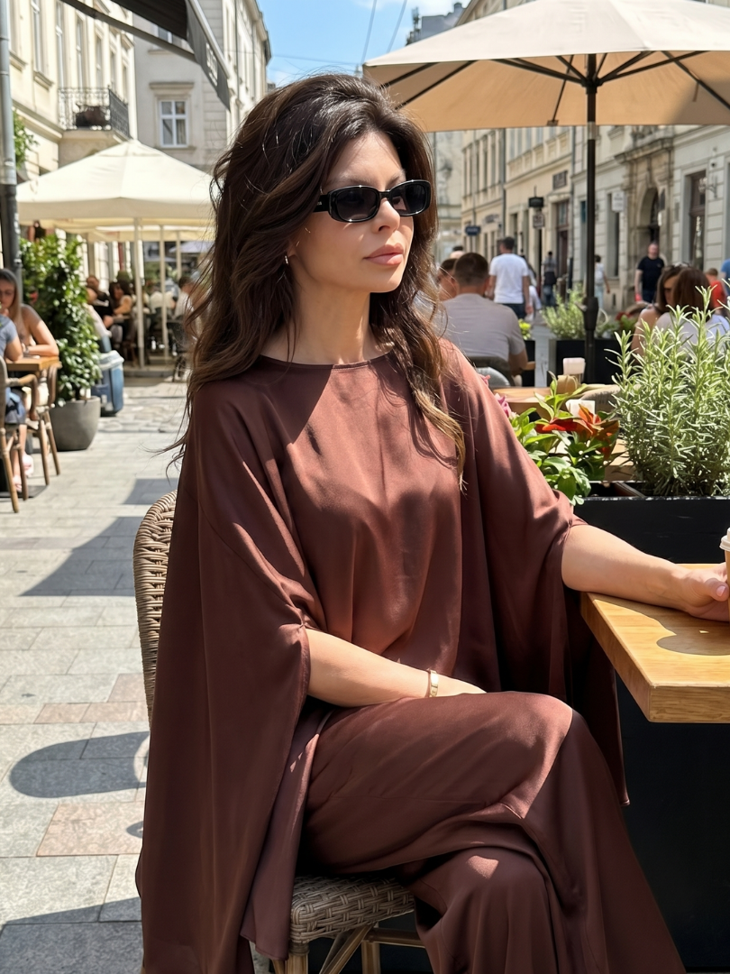 Brown asymmetrical two-piece set: draped top and wide-leg pants, seated street