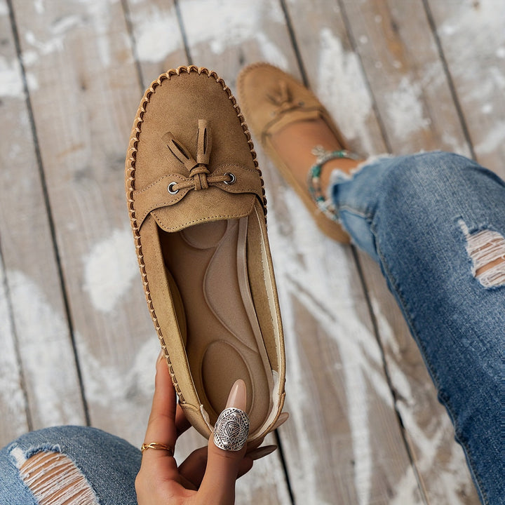 Caramel suede tassel loafers with bow detail and stitched moccasin edge, flat sole.