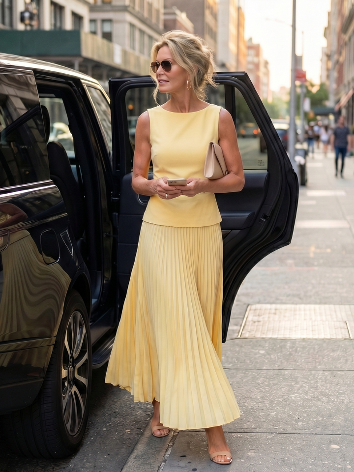 Yellow pleated two-piece set with sleeveless top and flowing pleated midi skirt