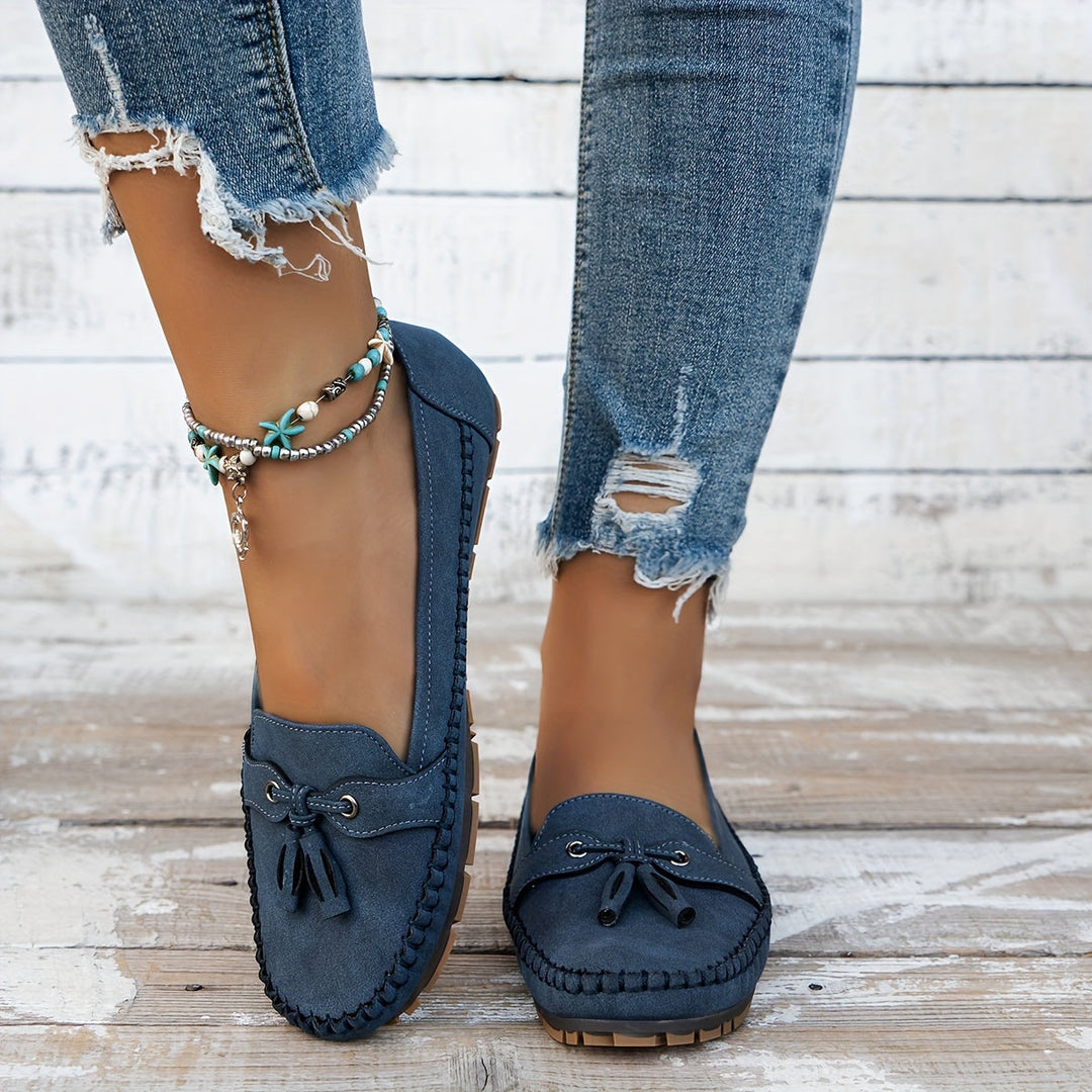 Blue suede tassel loafers with bow accents and moccasin stitching, flat low sole.