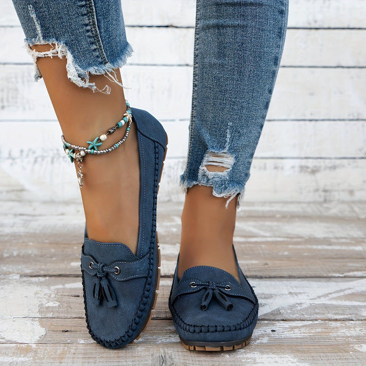 Blue suede tassel loafers with bow accents and moccasin stitching, flat low sole.
