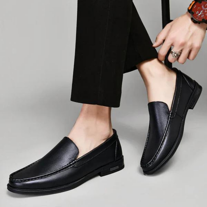 Black leather penny loafers worn by a person, stitched vamp and metal bit detail