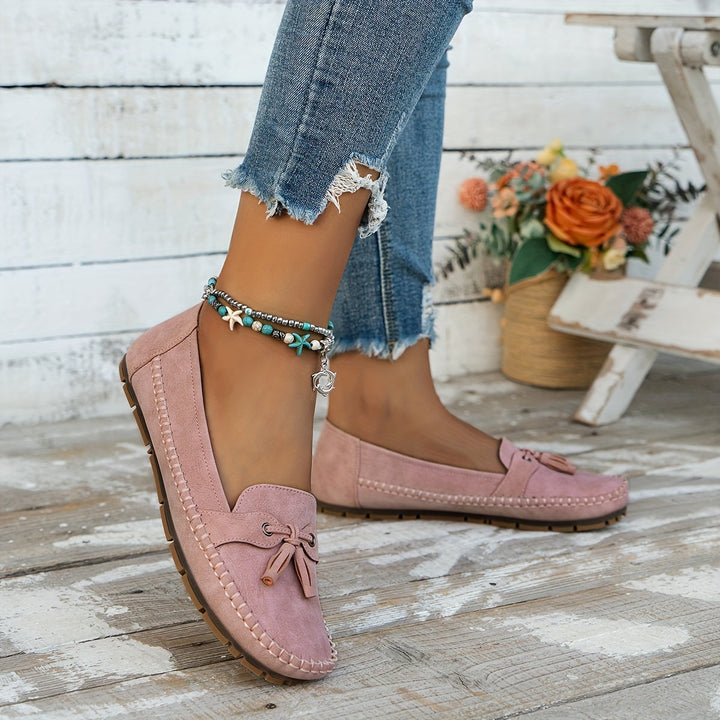 Pink suede tassel loafers with bow detail, stitched seams, and low flat sole.