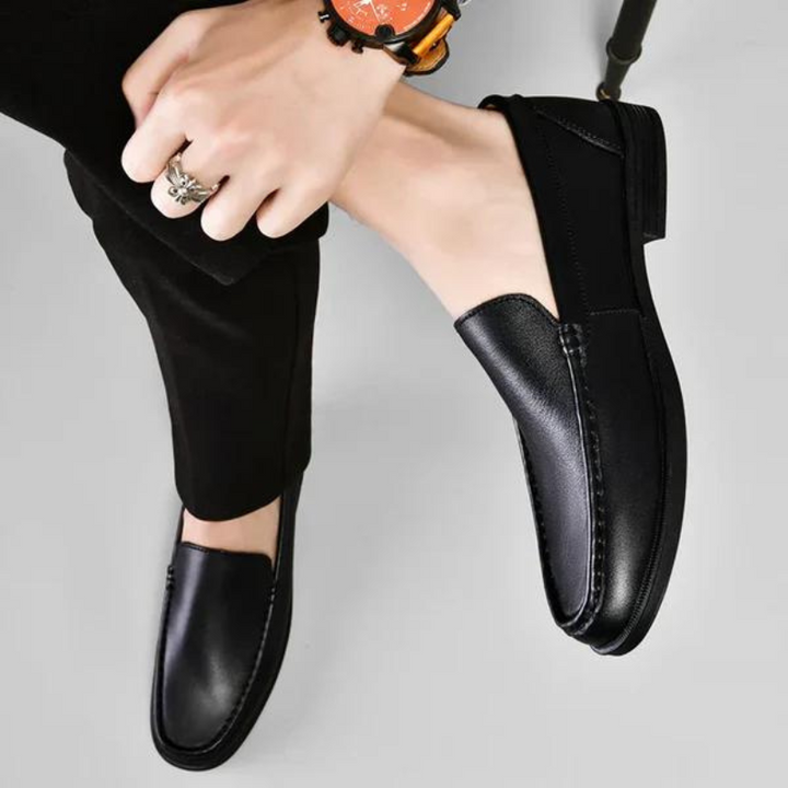 Black leather penny loafers shown on a person, stitched vamp and metal bit detail