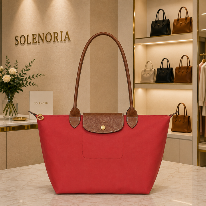 Medium tomato tote bag with brown leather handles, front pocket, and snap closure