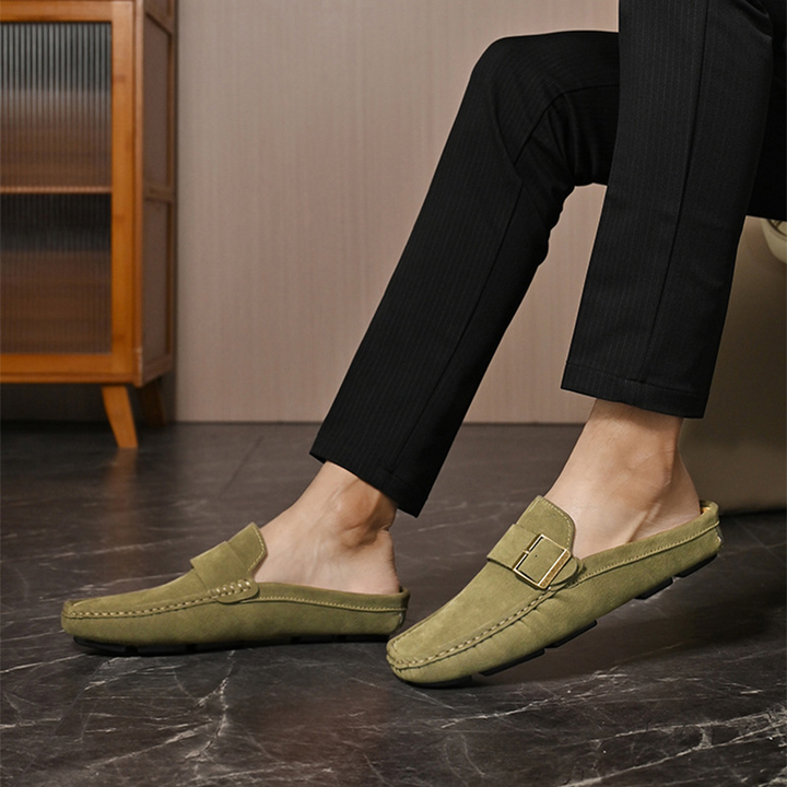 Olive suede loafers with front strap buckle, worn with dark pants