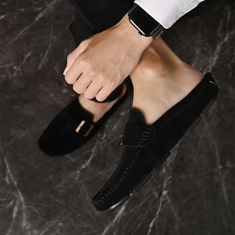 Black suede loafers with gold-tone buckle strap, hand adjusting a pair