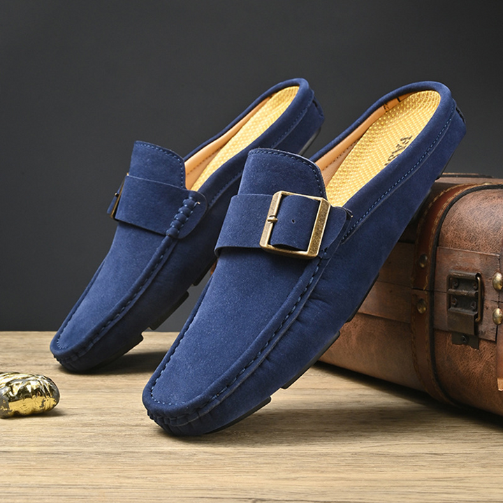 Pair of navy suede loafers with gold buckle strap and low-profile sole