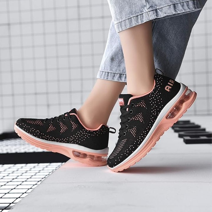 Black lace-up sneakers with orange trim and air-cushion soles on legs in jeans
