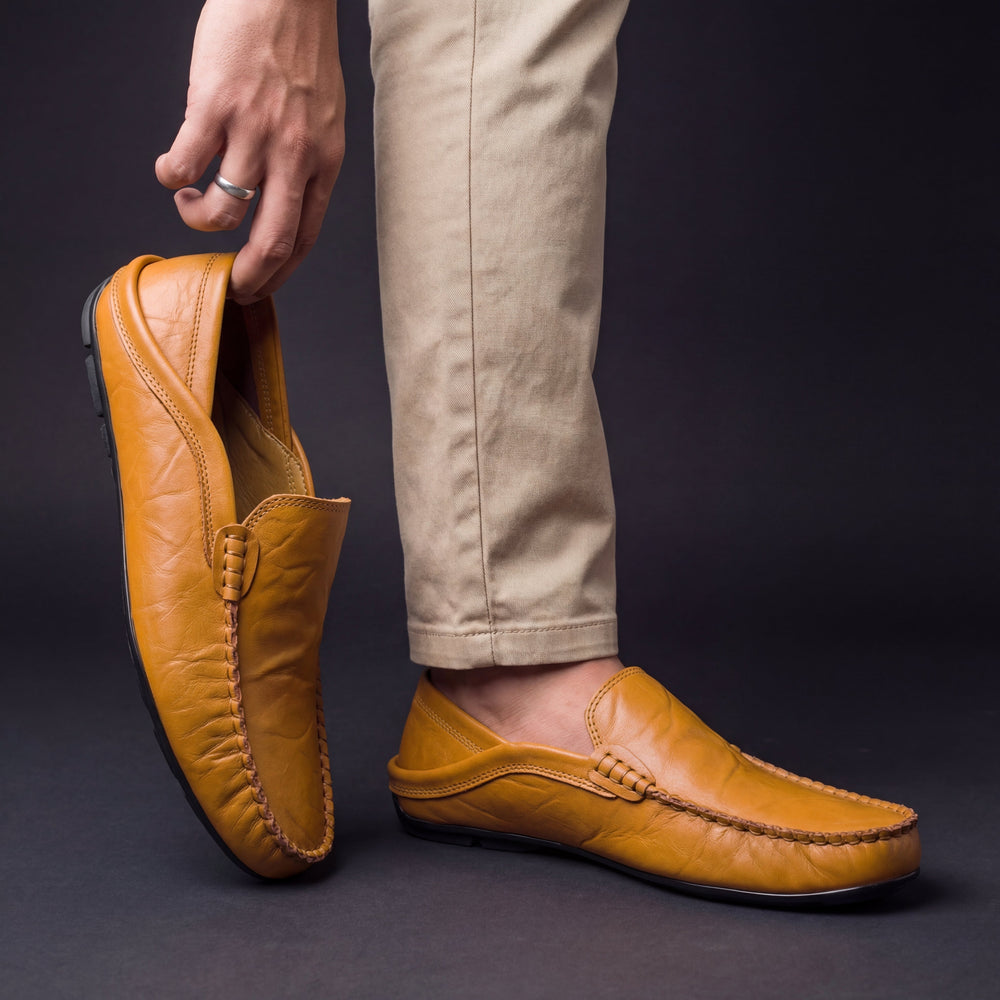 Tan leather loafer with moc toe stitching, slip-on design worn with pants