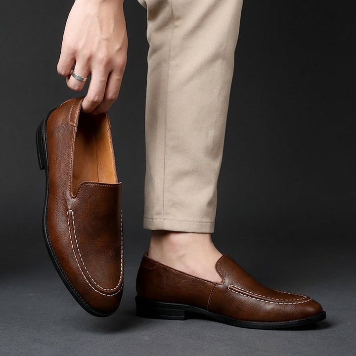 Brown slip-on loafers on feet with rounded toe and contrast-stitched apron