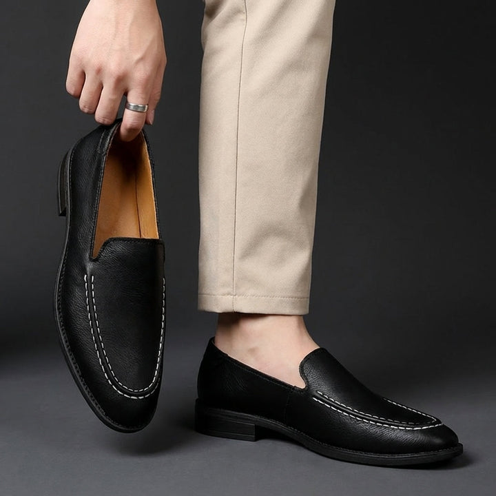 Black slip-on loafers on feet, rounded toe with contrast-stitched apron detail