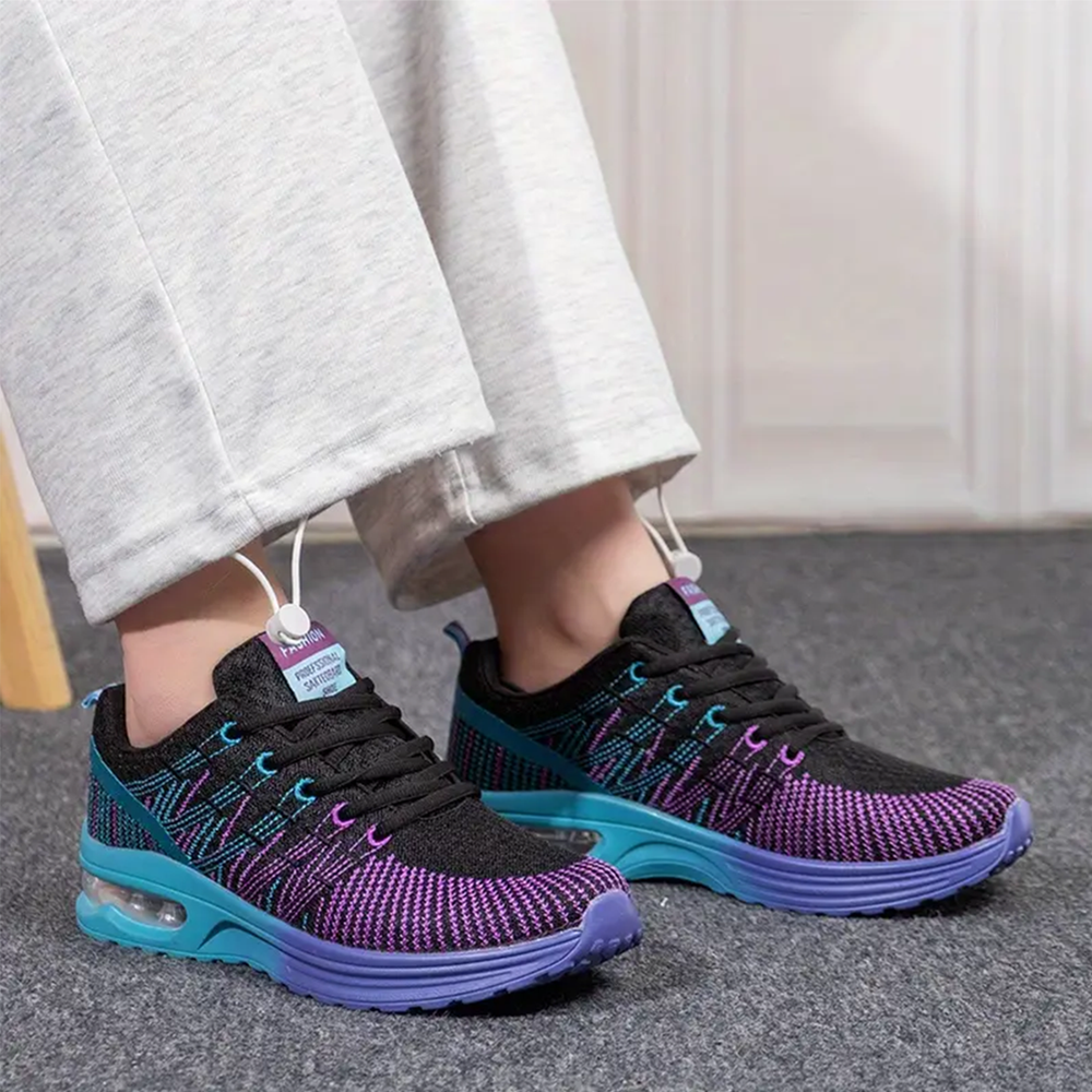 Walking sneakers on feet, black mesh upper with purple/teal print, blue outsole