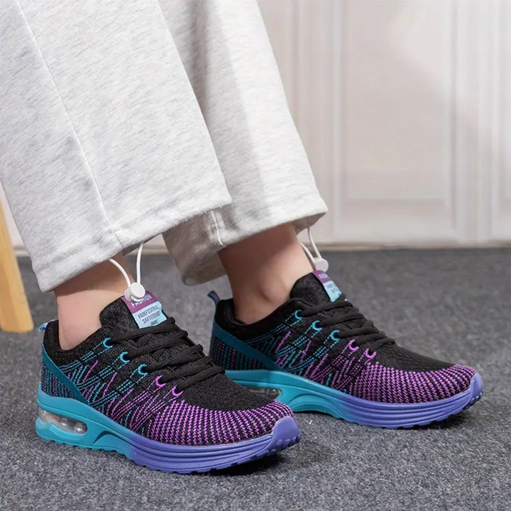 Walking sneakers on feet, black mesh upper with purple/teal print, blue outsole