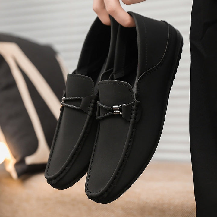 Black casual loafers worn by model, metal buckle and braided strap detail