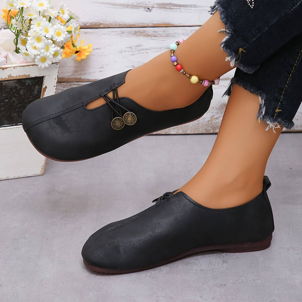 Black button slip-on flats with round logo medallion at vamp
