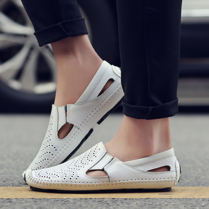 White slip-on sandals with perforations, cut-out sides, and tan sole trim on feet