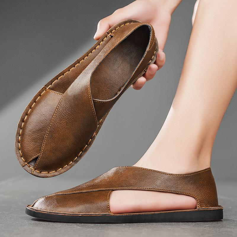 Brown leather open-toe slide sandal being held above a foot wearing the matching pair.