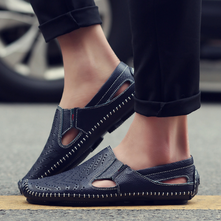 Navy perforated slip-on sandals worn with ankle-length pants, stitched edges