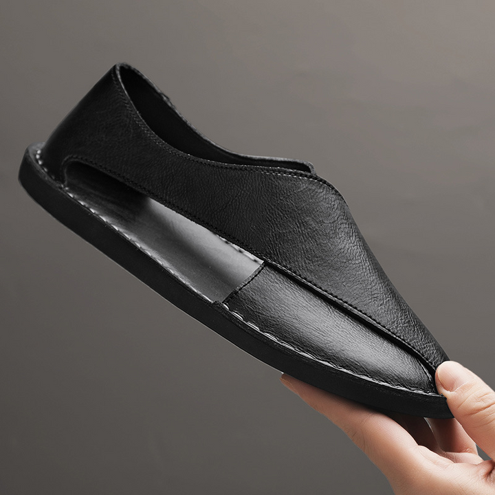 Black leather slip-on sandal held in hand, side seam and stitched edge detailing