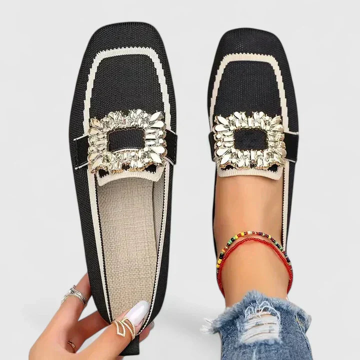 Black square-toe flats with white trim and ornate gold jeweled buckle