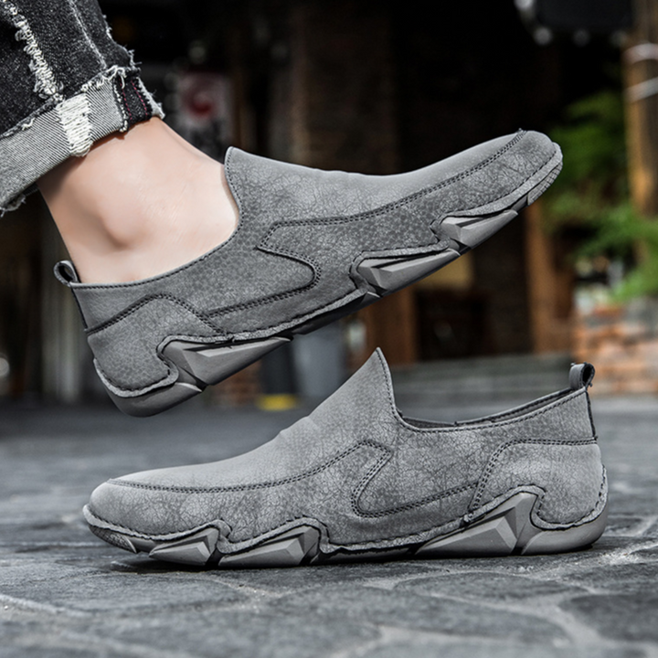 Gray slip-on loafers on model foot, moc-toe stitching and chunky rubber sole.