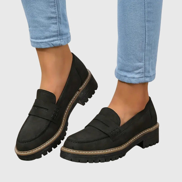 Black chunky slip-on loafers with side strap and tan edge trim, thick tread sole