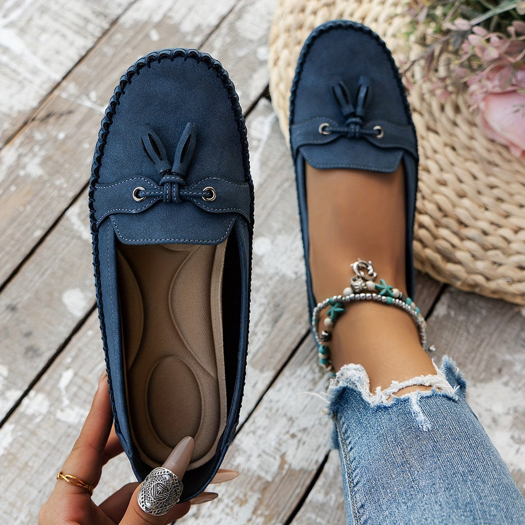 Dark blue suede tassel loafers with bow detail and stitched moccasin edging, flat sole.