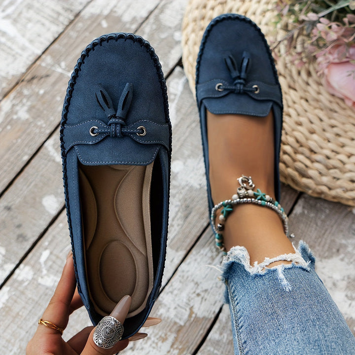 Dark blue suede tassel loafers with bow detail and stitched moccasin edging, flat sole.