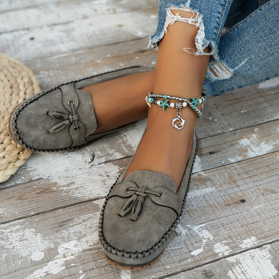 Gray suede tassel loafers with bow accent and stitched moccasin edge, low flat sole.