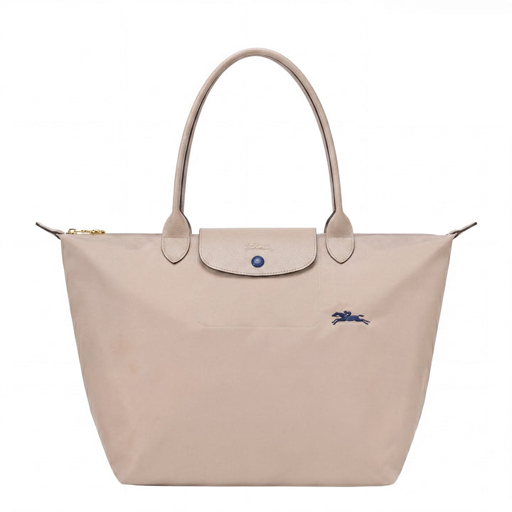 Light beige tote bag with flap front, blue button, and small blue logo detail